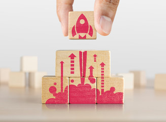 Wall Mural - Business start up, start, new project or new idea concept. Wooden blocks with launching rocket graphic arranged in pyramid shape and a man is holding the top one.