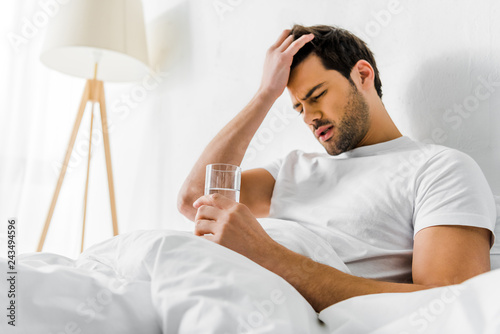 Cuadros en Lienzo tired man with headache holding glass of water in bed in the morning