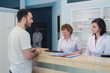 © romankosolapov - Qualified smiling doctors working with client at reception desk in hospital