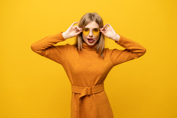 Wall Mural - Excited young woman in orange dress, widely smiling, looking at camera. Isolated on yellow background