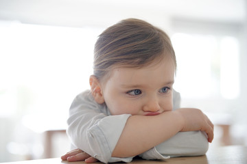 Portrait of adorable girl indoors with arms crossed on table