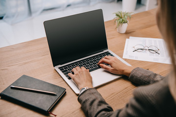 cropped view of businesswoman typing on laptop at workplace with documents