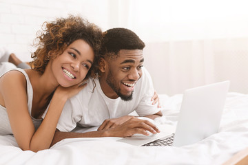 Young black couple lying on bed and using laptop.