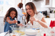 © Monkey Business - Young girl making cake in the kitchen with her mum, grandmother busy in background, selective focus