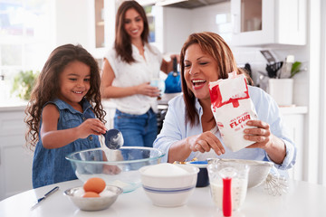 Wall Mural - Young girl making a cake in the kitchen with her grandmother, mum stands watching, selective focus