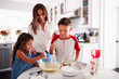 © Monkey Business - Brother and sister making cake mixture together at the kitchen table with their mum, waist up