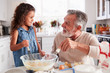 © Monkey Business - Young girl and grandfather making cake mixture at the kitchen table, smiling at each other, close up