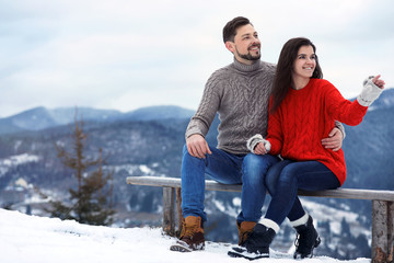  Couple sitting on bench in mountains, space for text. Winter vacation