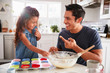 © Monkey Business - Young girl stands at the kitchen table making cakes with her father, tasting the cake mix, close up