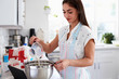 © Monkey Business - Millennial Hispanic woman pouring milk into cake mixture, following a recipe on her tablet computer