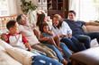 © Monkey Business - Three generation Hispanic family sitting on the sofa watching TV, grandmother using remote control