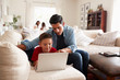 © Monkey Business - Pre-teen boy lying on sofa using laptop, dad sitting beside him, mum and sister in the background