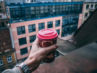 partial view of man holding disposable cup of coffee with blurred city on background