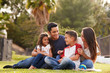 © Monkey Business - Happy young Hispanic family sitting together on the grass in the park, looking at each other
