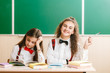 © slavonstok - two brunette schoolgirls sit in the classroom at her desk with books on the background of the blackboard