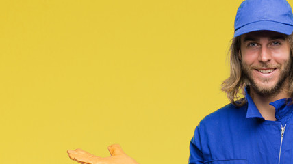 Sticker - Young handsome mechanic man with long hair over isolated background amazed and smiling to the camera while presenting with hand and pointing with finger.