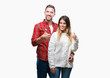 © Krakenimages.com - Young couple in love wearing winter sweater over isolated background doing happy thumbs up gesture with hand. Approving expression looking at the camera with showing success.