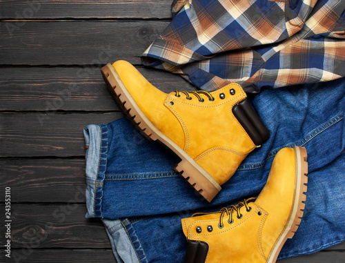Fotografía Men's casual wear, yellow work boots from natural nubuck leather, blue jeans, checkered shirt and brown belt on dark wooden background top view flat lay copy space