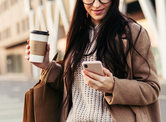 Young trendy woman blogger with shopping bag and smartphone near mall