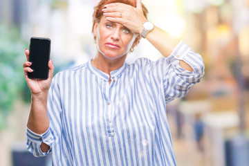 Sticker - Atrractive senior caucasian redhead woman showing smartphone screen over isolated background stressed with hand on head, shocked with shame and surprise face, angry and frustrated. Fear and upset