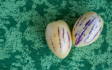 two ripe yellow pepino melons on a green tropical pattern cloth with copy space