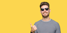 Young Handsome Man Wearing Sunglasses Doing Happy Thumbs Up Gesture With Hand. Approving Expression Looking At The Camera With Showing Success.