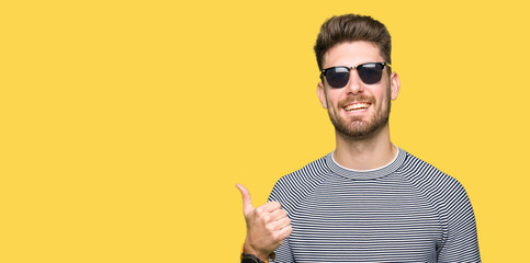 Young handsome man wearing sunglasses doing happy thumbs up gesture with hand. Approving expression looking at the camera with showing success.