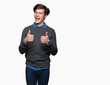 © Krakenimages.com - Young handsome elegant man over isolated background success sign doing positive gesture with hand, thumbs up smiling and happy. Looking at the camera with cheerful expression, winner gesture.