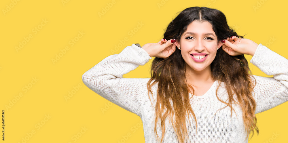 Young beautiful woman wearing white sweater Smiling pulling ears with fingers, funny gesture. Audition problem