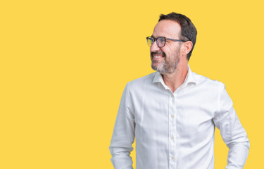 Handsome middle age elegant senior business man wearing glasses over isolated background looking away to side with smile on face, natural expression. Laughing confident.