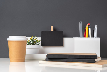 Poster - modern office stationery on white table and dark grey wall.pencil,ruler,pen,pencil box,coffee cup and blackboard with plant.Mock up paper note for display of design or content.