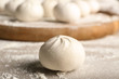 © Pixel-Shot - Uncooked steamed bun dough ball on floured surface with blurred background of more buns and wooden board, raw stage of making traditional asian steamed buns, the texture and form of the dough