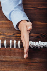 top view of man preventing dominoes from falling on wooden desk