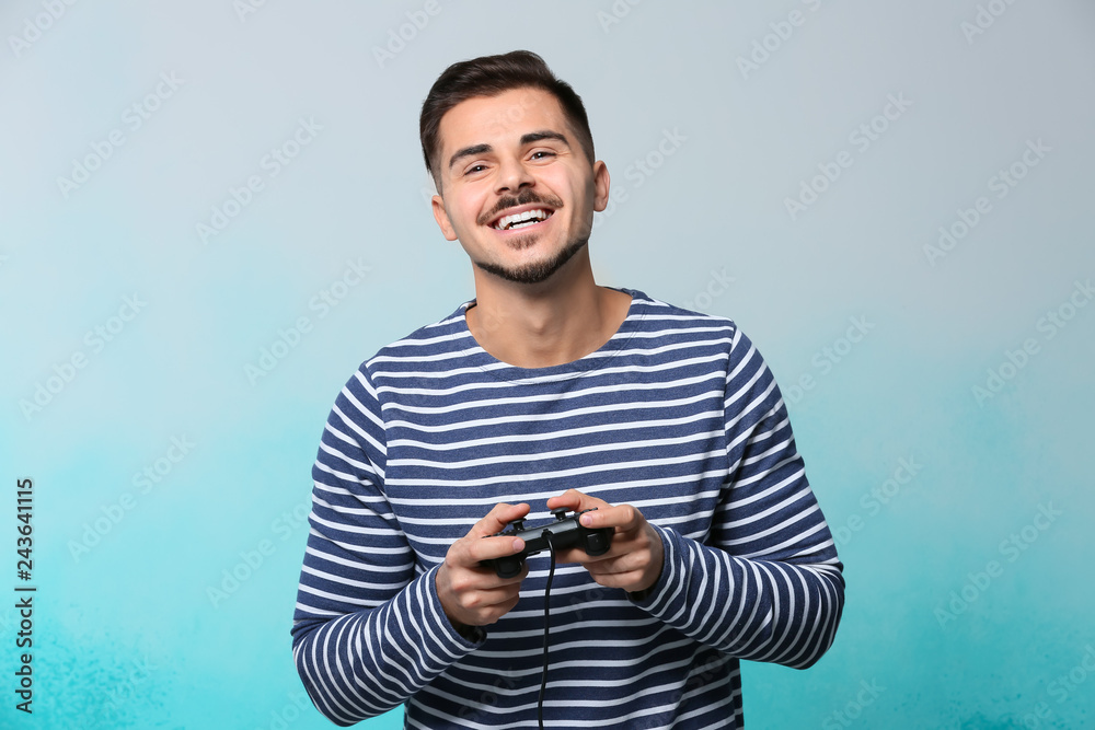 Happy young man playing video game on color background