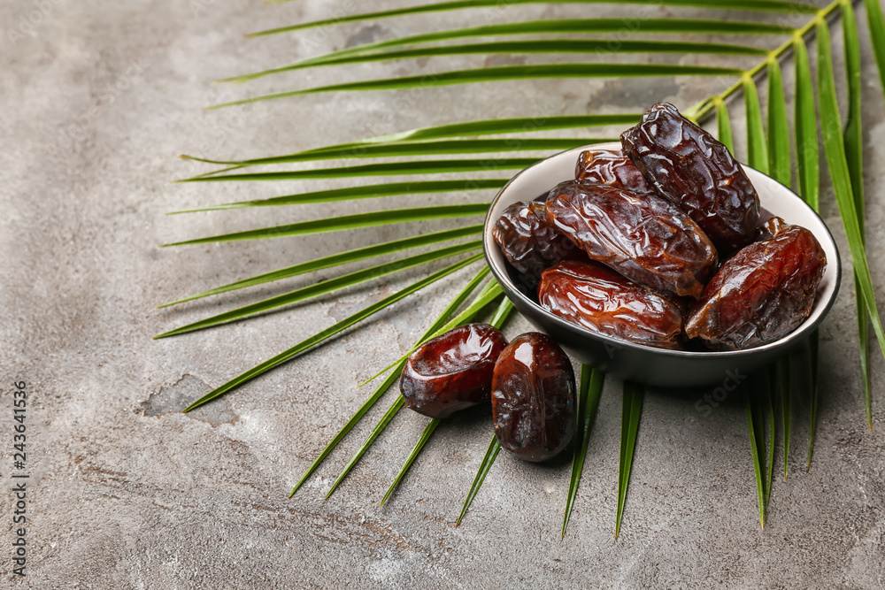 Bowl with sweet dried dates on grey background