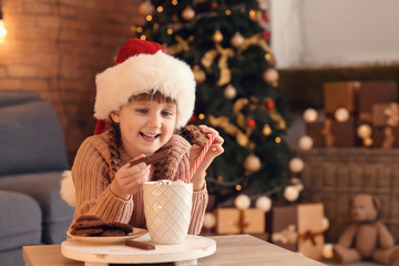 Wall Mural - Cute little girl in Santa hat drinking hot chocolate and eating cookies at home on Christmas eve