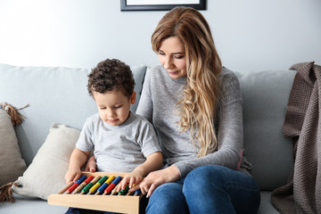 Young mother with cute little son playing with abacus at home