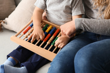 Young mother with cute little son playing with abacus at home