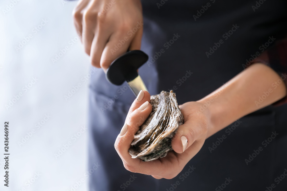 Woman opening raw oyster with knife, closeup