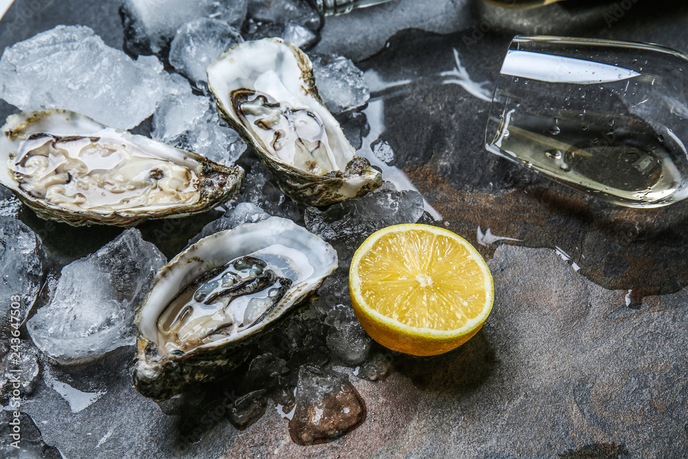 Tasty raw oysters with ice, lemon and white wine on grey background