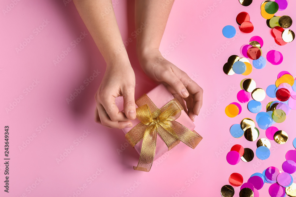 Female hands with beautiful gift box and confetti on color background