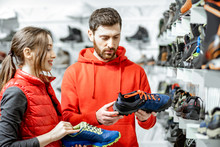 Mam And Woman In Red Sports Clothes Choosing Trail Shoes For Hiking Standing Near The Showacase Of The Modern Sports Shop