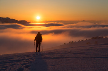 Hiker walking on snowshoes in the snow-covered mountains during a colorful, winter sunset. Vercors, France.