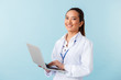 © Drobot Dean - Young woman doctor posing isolated over blue wall background using laptop computer.