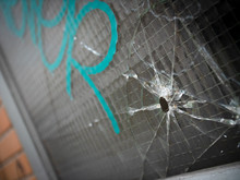 Bullet Hole And Cracks In A Reinforced Window With Gang Graffiti