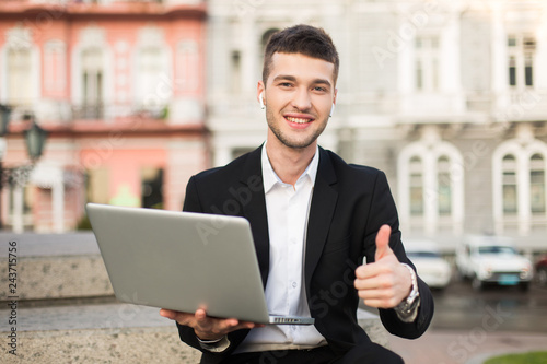 Photographie Young smiling businessman in classic black suit and white shirt with wireless ea