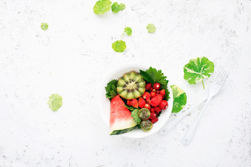 Wall Mural - Fruit salad. Watermelons, strawberries, kiwi, nasturtium leaves for pure nutrition. On a light background. Top view.