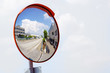 Outdoor convex safety mirror hanging on wall with reflection of an urban roadside view of cars parked along the street by residential apartment buildings.
