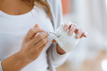 Woman's hand holding yogurt while eating at home.