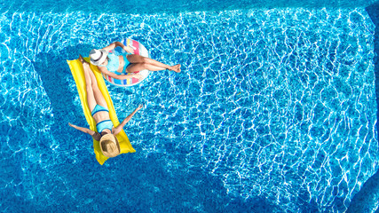 Children in swimming pool aerial drone view fom above, happy kids swim on inflatable ring donut and mattress, active girls have fun in water on family vacation on holiday resort
